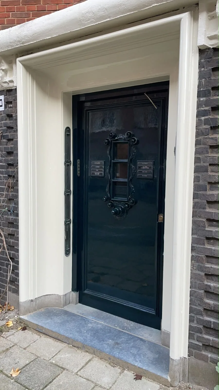 Donkergroene voordeur hoogglans gelakt in een bakstenen gevel in Amsterdam